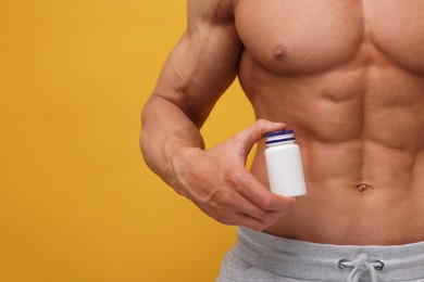 Photo of Weight loss. Athletic man with bottle of supplements on orange background, closeup. Space for text