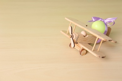 Wooden airplane with cute Easter egg on table, space for text