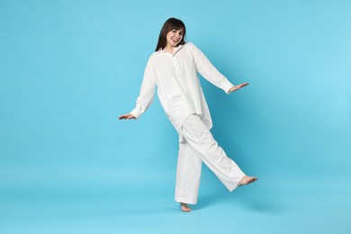 Photo of Happy woman wearing pyjama on light blue background