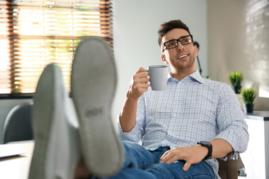 Young man with cup of drink relaxing at workplace