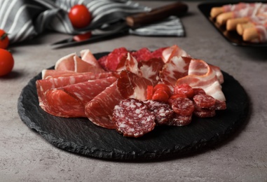 Photo of Slate plate with different meat delicacies on gray table