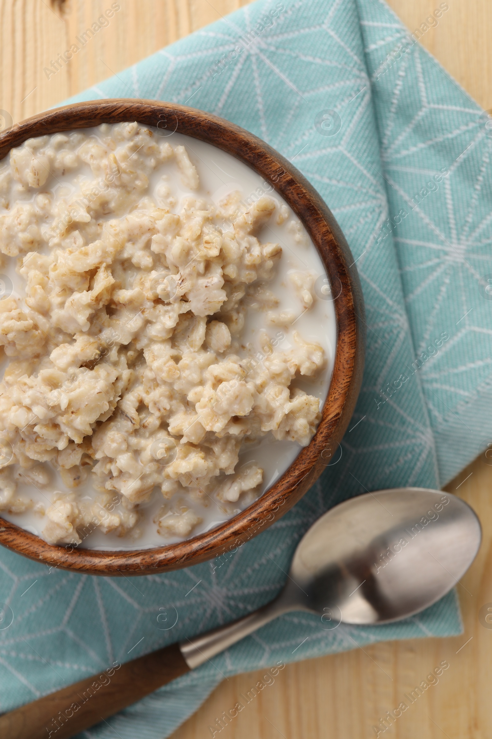 Photo of Tasty boiled oatmeal in bowl and spoon on wooden table, top view