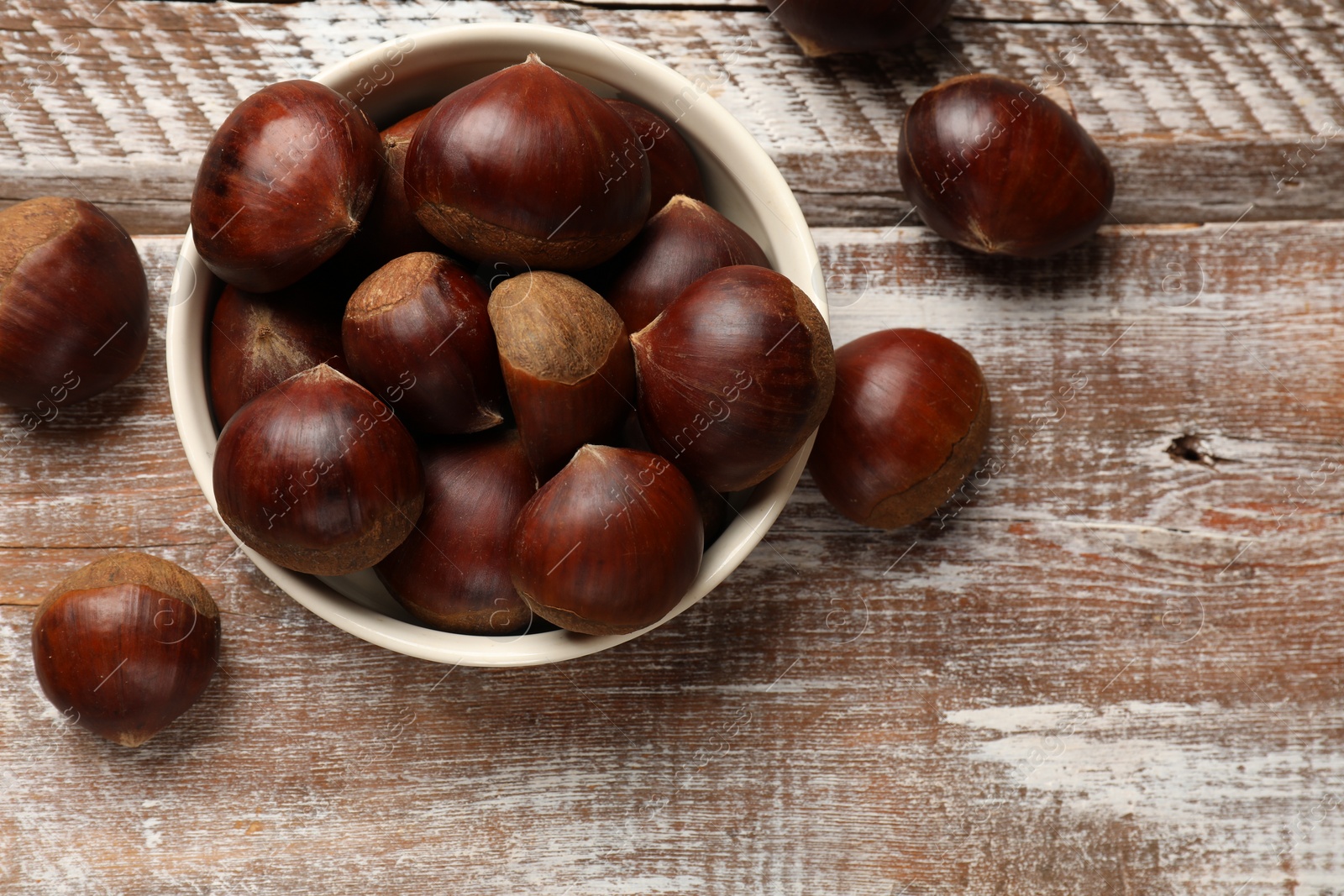 Photo of Sweet fresh edible chestnuts in bowl on wooden table, top view