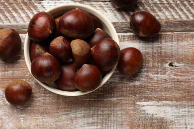 Sweet fresh edible chestnuts in bowl on wooden table, top view