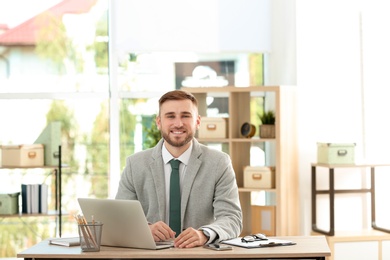 Photo of Young handsome man working with laptop at table in office
