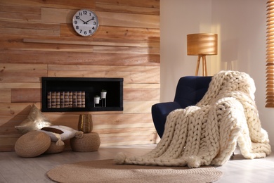 Soft knitted blanket on armchair in living room. Interior element