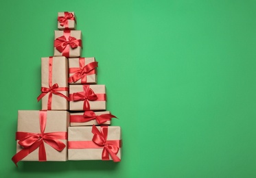 Photo of Christmas tree shape of gift boxes on green background, flat lay. Space for text