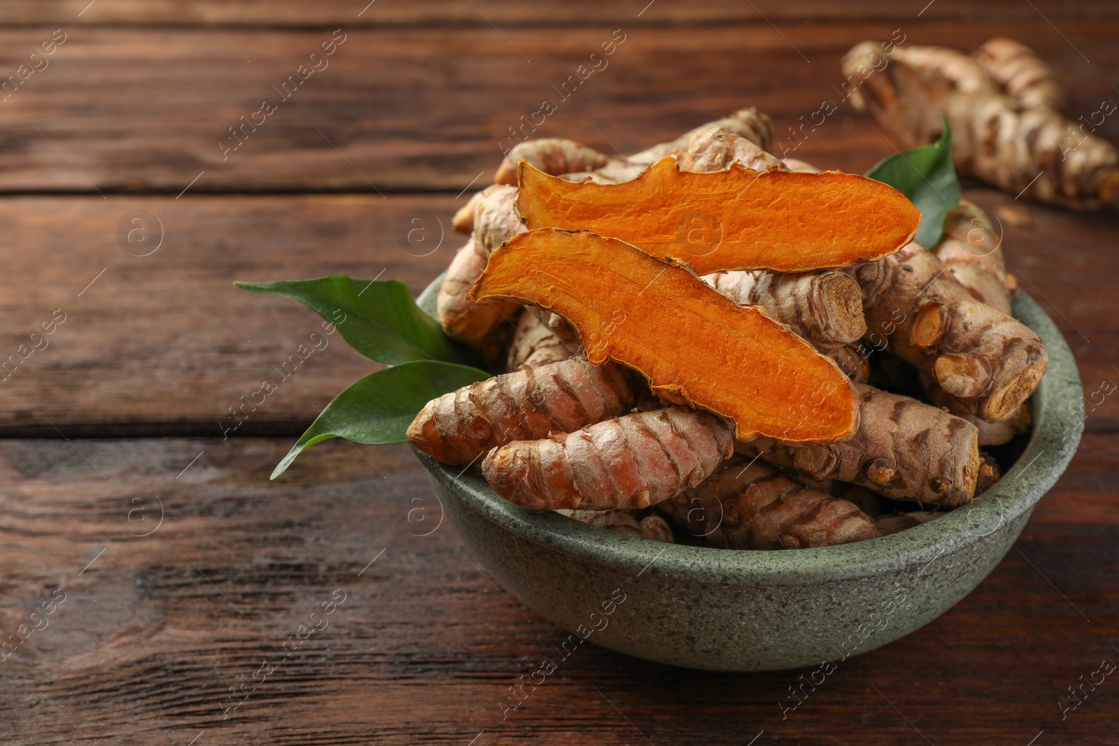 Photo of Bowl with fresh turmeric roots on wooden table. Space for text