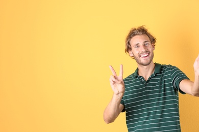 Handsome young man laughing and taking selfie on color background. Space for text