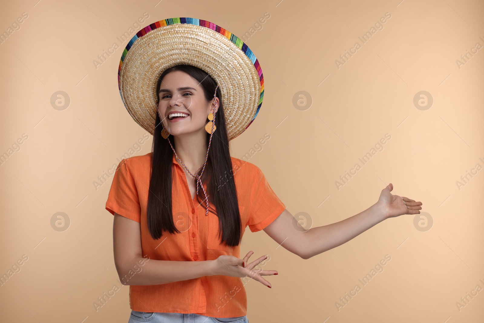 Photo of Young woman in Mexican sombrero hat showing something on beige background