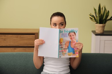 Photo of Young woman with magazine sitting on sofa