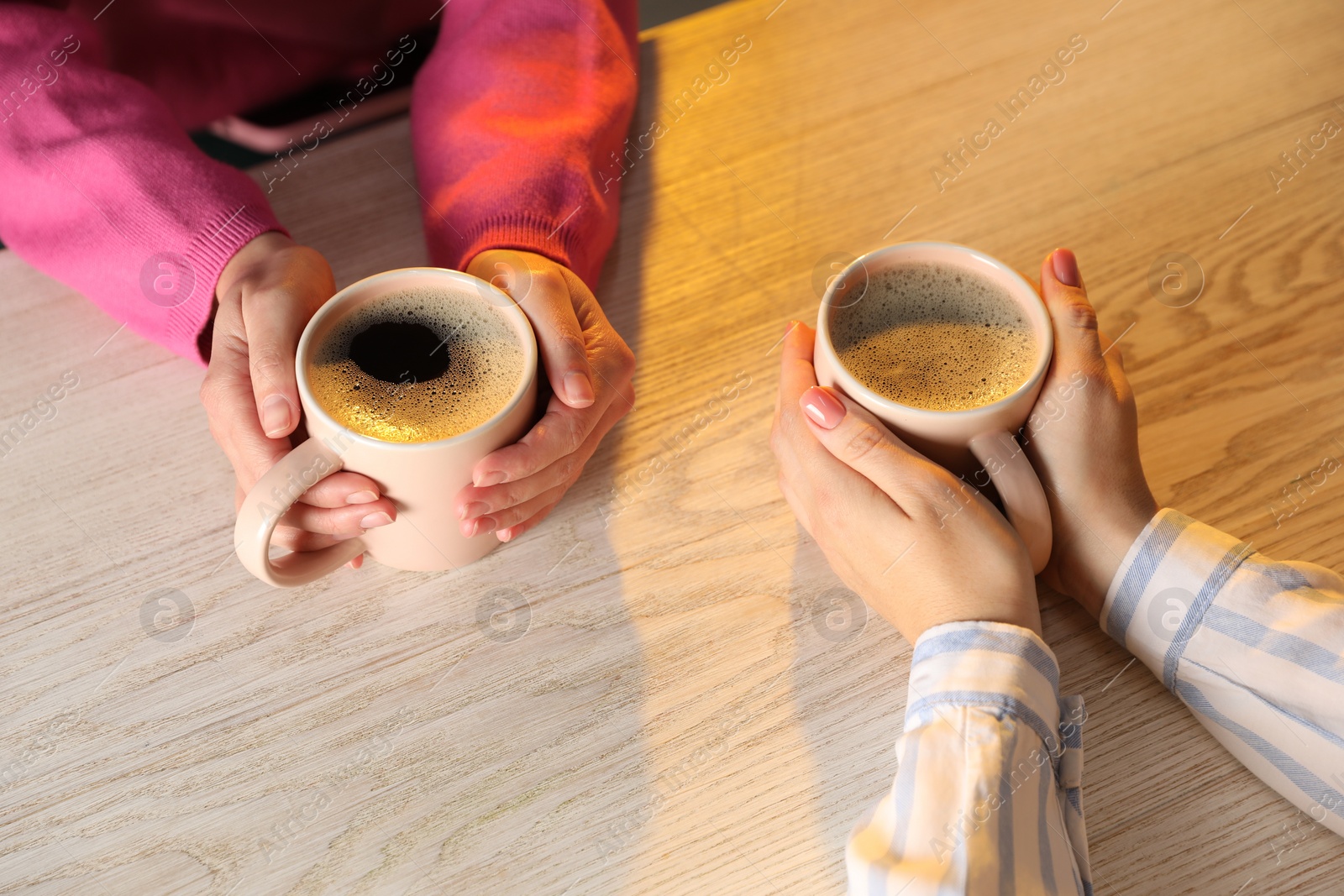 Photo of Women with cups of hot coffee at light wooden table, closeup