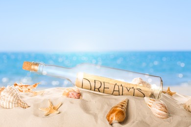 Image of Corked glass bottle with rolled paper note and seashells on sandy beach near ocean