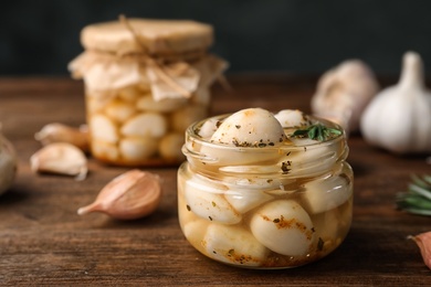 Photo of Preserved garlic in glass jar on wooden table, closeup