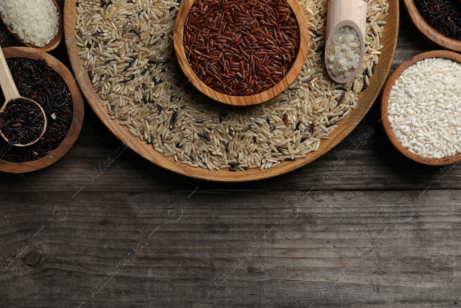 Photo of Different sorts of rice on wooden table, flat lay. Space for text