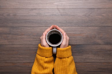 Photo of Woman with cup of coffee at wooden table, top view