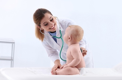 Photo of Children's doctor examining baby with stethoscope in hospital. Space for text