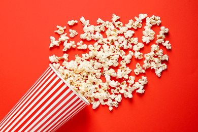 Photo of Overturned paper cup with delicious popcorn on red background, top view