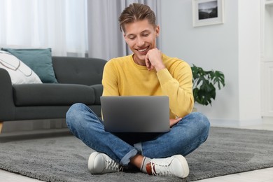 Photo of Happy young man having video chat via laptop on carpet indoors