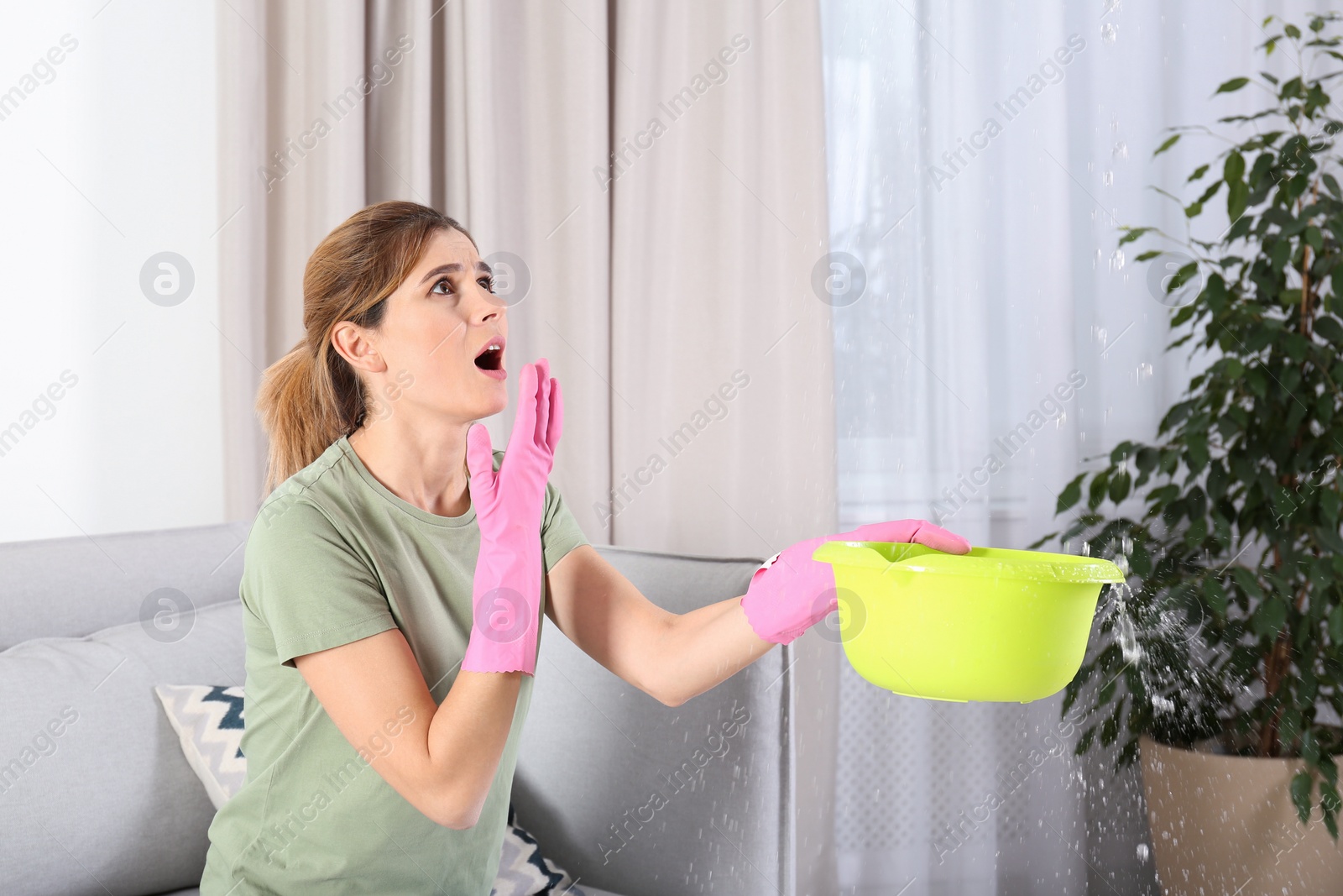 Photo of Woman collecting leaking water from ceiling in living room. Time to call plumber