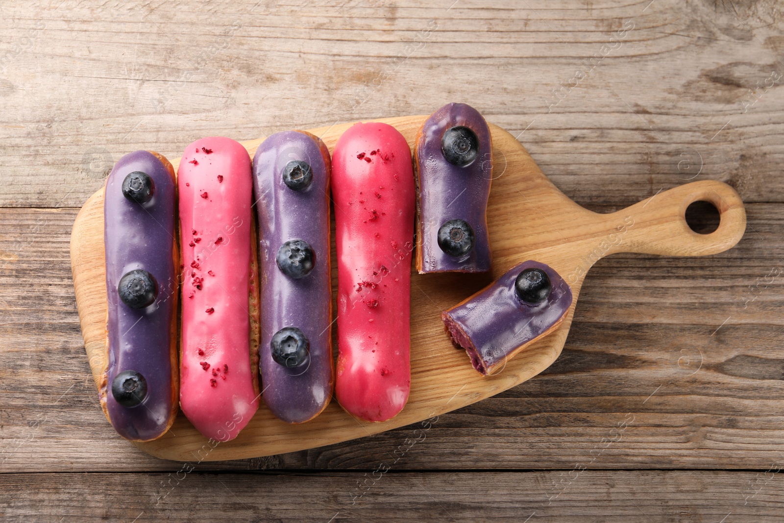 Photo of Different tasty glazed eclairs on wooden table, top view