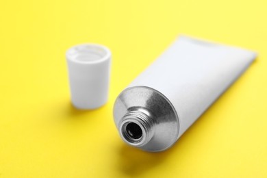 Photo of Open white tube of ointment on yellow background, closeup