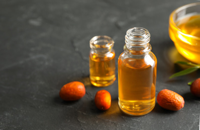 Jojoba oil and seeds on dark grey table