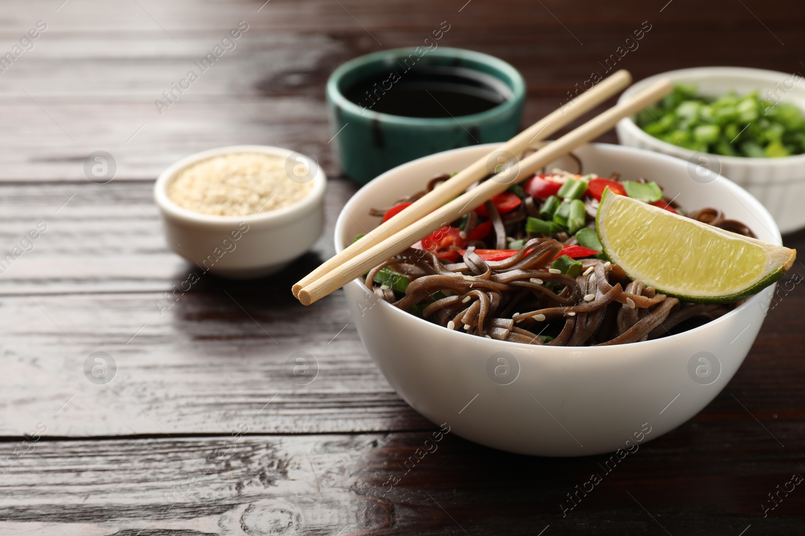 Photo of Tasty buckwheat noodles (soba) with chili pepper and lime served on wooden table, closeup. Space for text