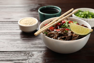 Photo of Tasty buckwheat noodles (soba) with chili pepper and lime served on wooden table, closeup. Space for text