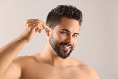 Photo of Handsome man applying cosmetic serum onto face on light grey background