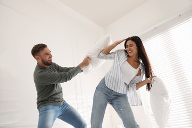 Photo of Happy young couple having fun pillow fight at home