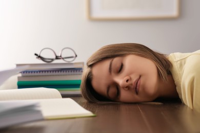 Young tired woman sleeping near books at wooden table indoors, closeup