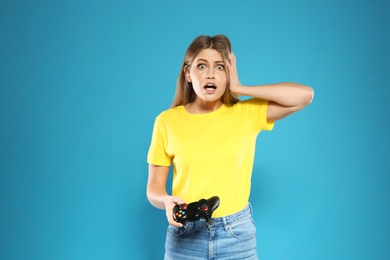 Photo of Emotional young woman playing video games with controller on color background