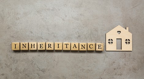 Photo of Word Inheritance made with wooden cubes and house model on grey background, flat lay