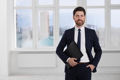 Photo of Happy real estate agent with leather portfolio indoors. Space for text