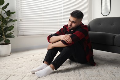 Photo of Sad man sitting on floor at home. Space for text