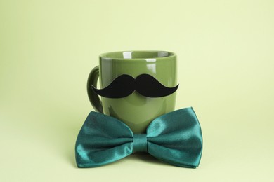 Photo of Man's face made of cup, fake mustache and bow tie on light green background