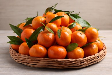 Photo of Fresh ripe juicy tangerines and green leaves on white wooden table