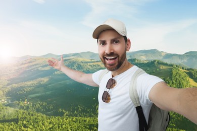 Image of Smiling man taking selfie in mountains on sunny morning