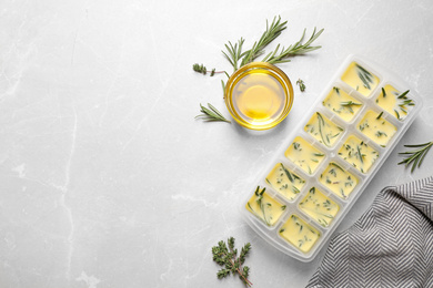 Ice cube tray with herbs frozen in oil and fresh rosemary on grey table, flat lay. Space for text