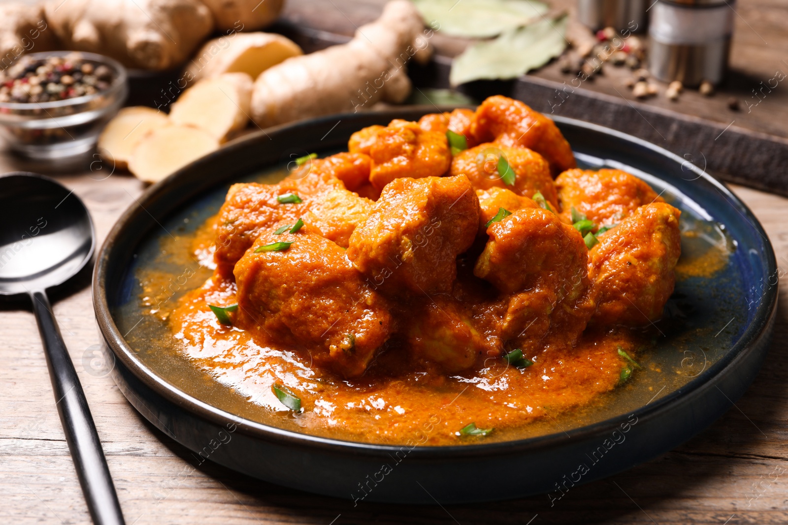 Photo of Plate of delicious chicken curry on wooden table, closeup