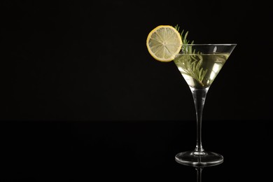 Martini cocktail with lemon slice and rosemary on black background, space for text