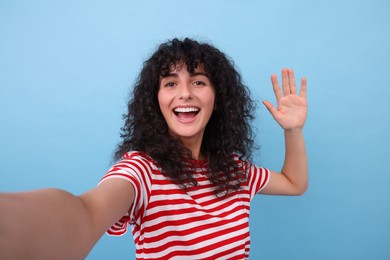 Beautiful young woman taking selfie on light blue background