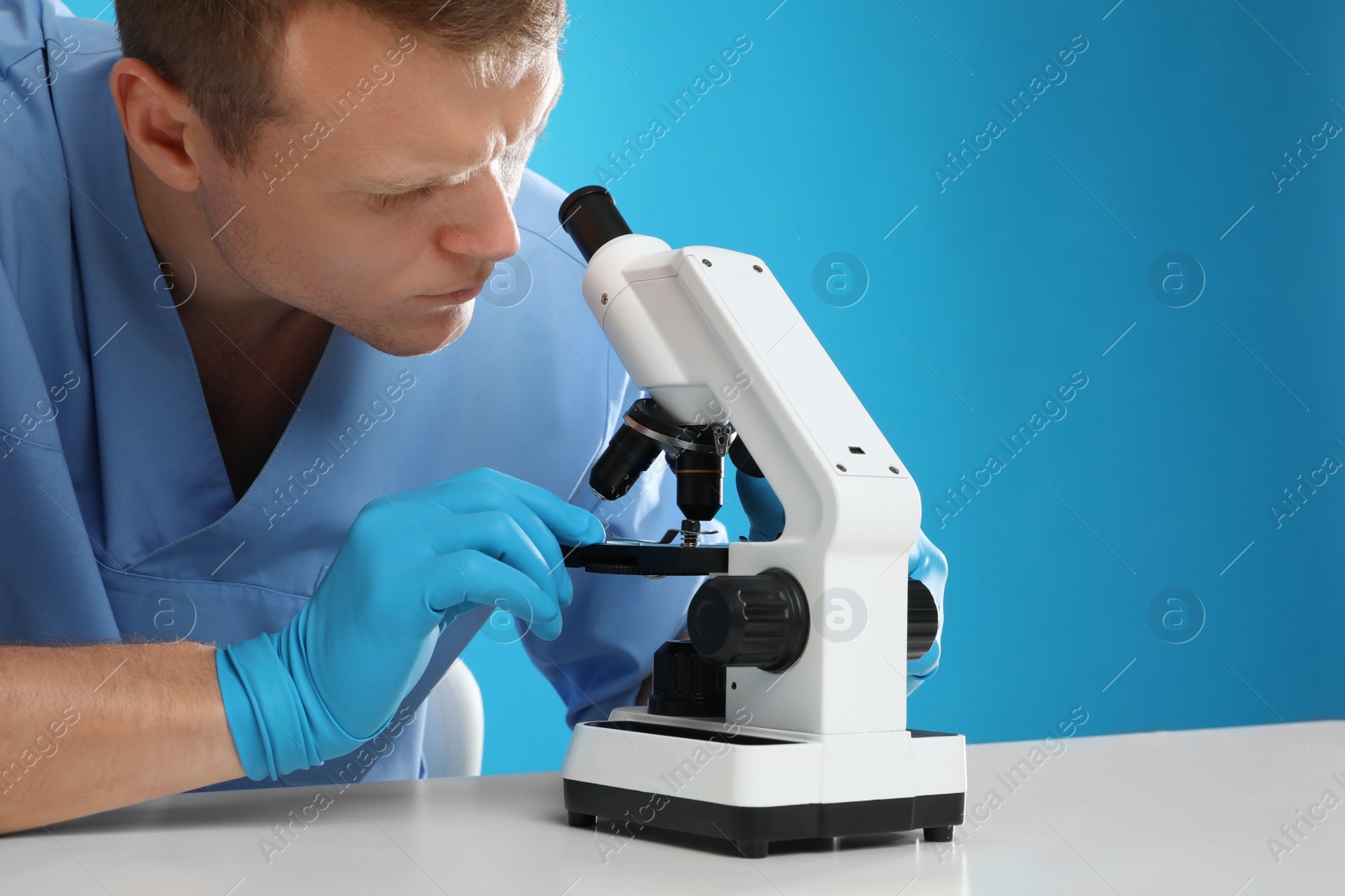 Photo of Scientist using modern microscope at table against blue background, closeup. Medical research