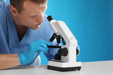 Photo of Scientist using modern microscope at table against blue background, closeup. Medical research