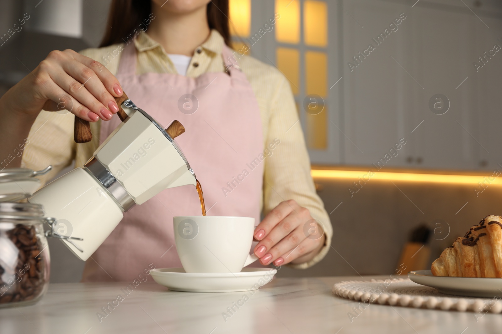 Photo of Woman pouring aromatic coffee from moka pot into cup at white marble table, closeup