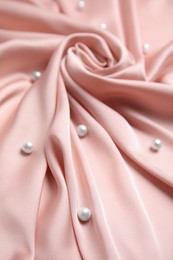 Many beautiful pearls on delicate pink silk, closeup