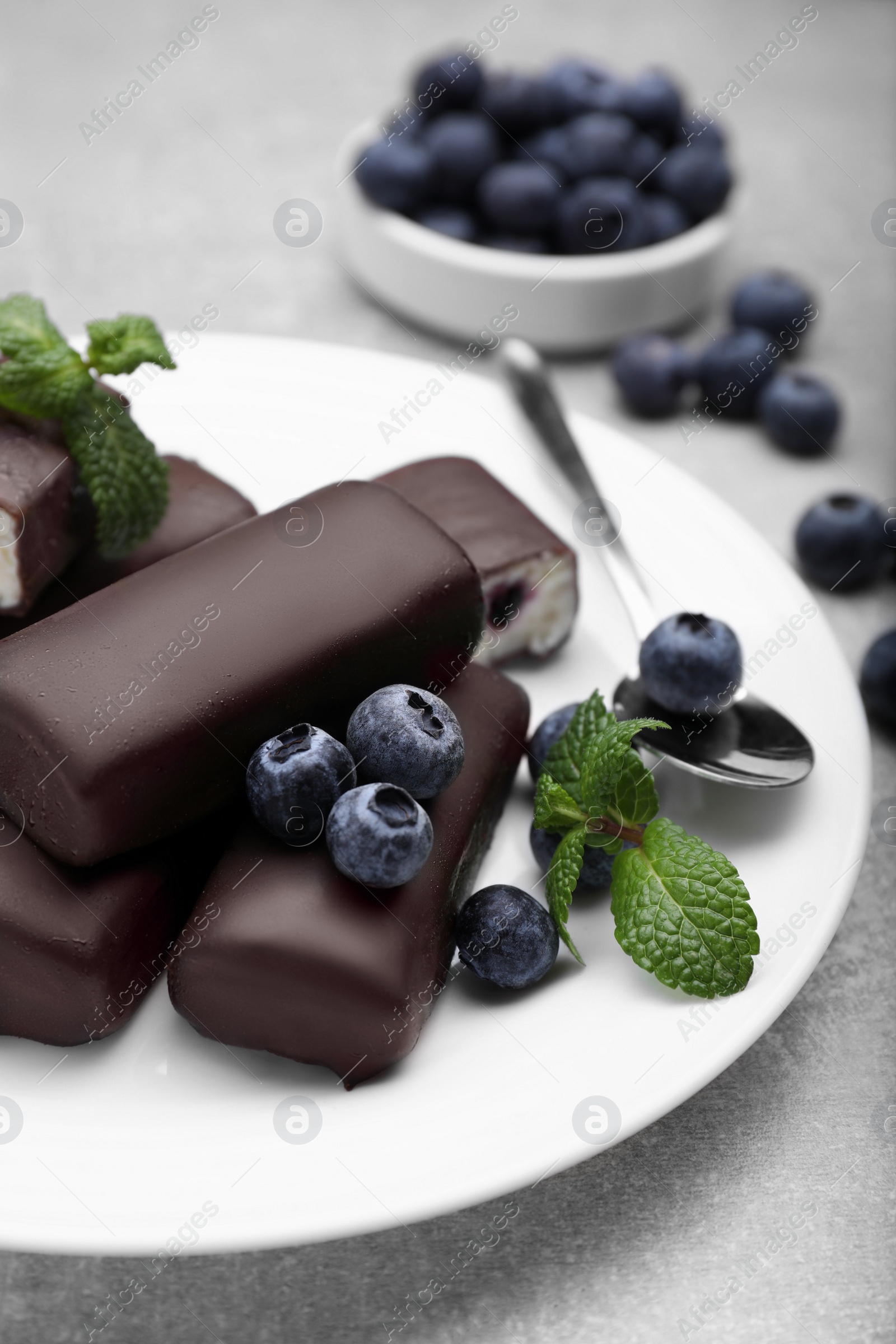 Photo of Delicious glazed curd snacks with fresh blueberries and mint on light grey table