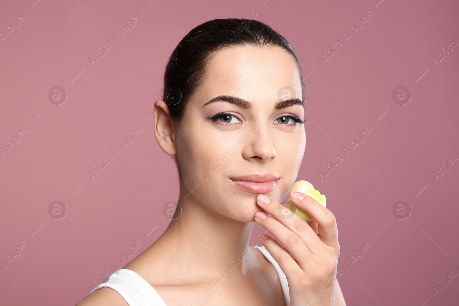 Photo of Young woman applying balm on her lips against color background