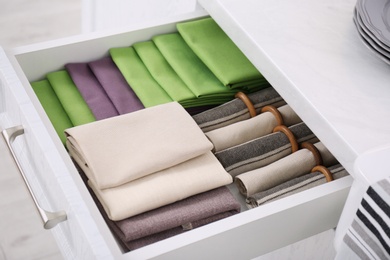 Photo of Open drawer with different folded towels and napkins in kitchen, closeup